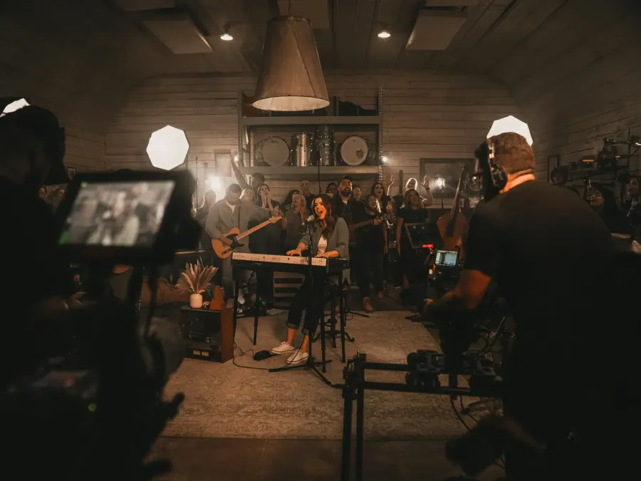 A band recording in a warm-lit studio, a camera in the foreground.